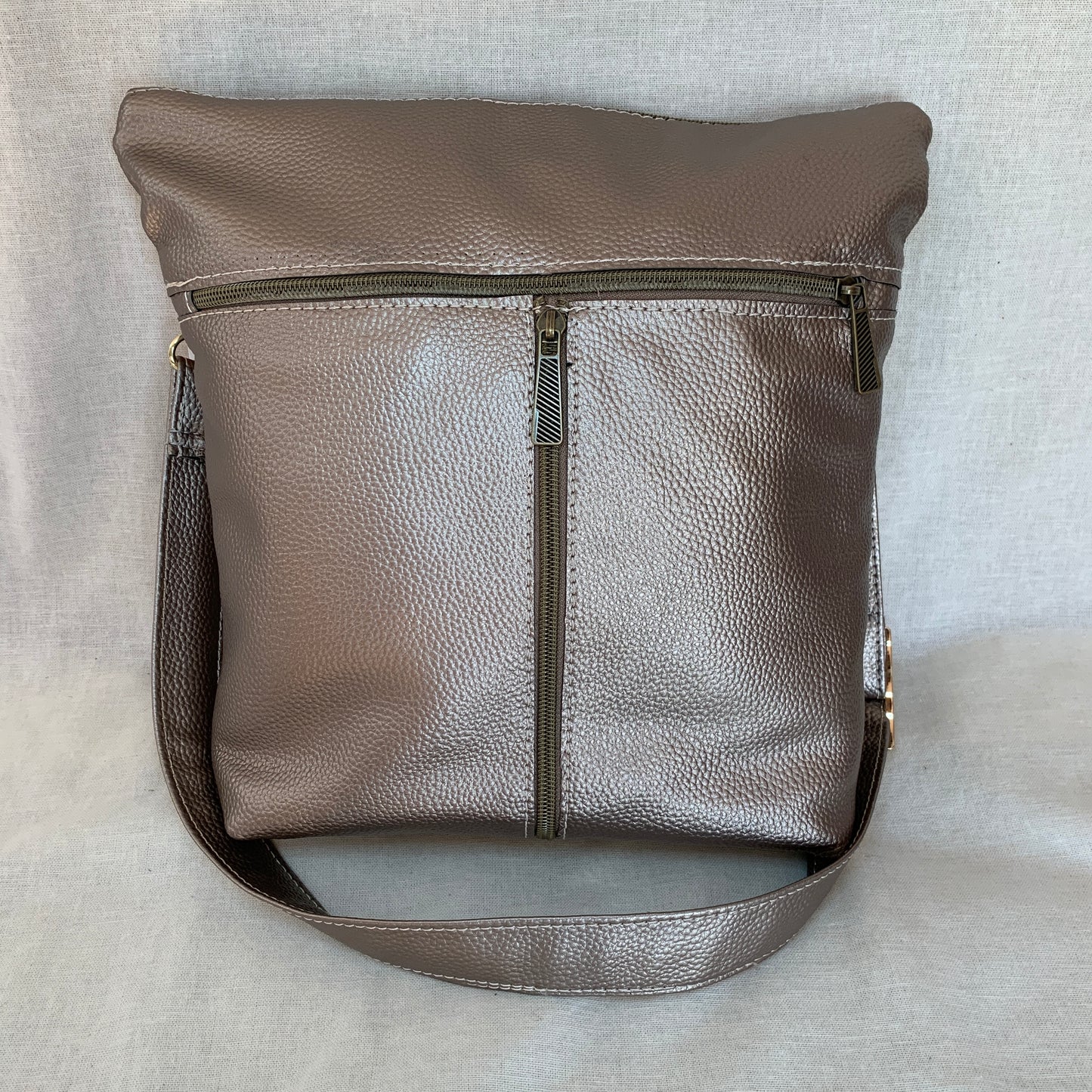 Metallic vinyl crossbody with exterior slip pockets and interior zip pockets.