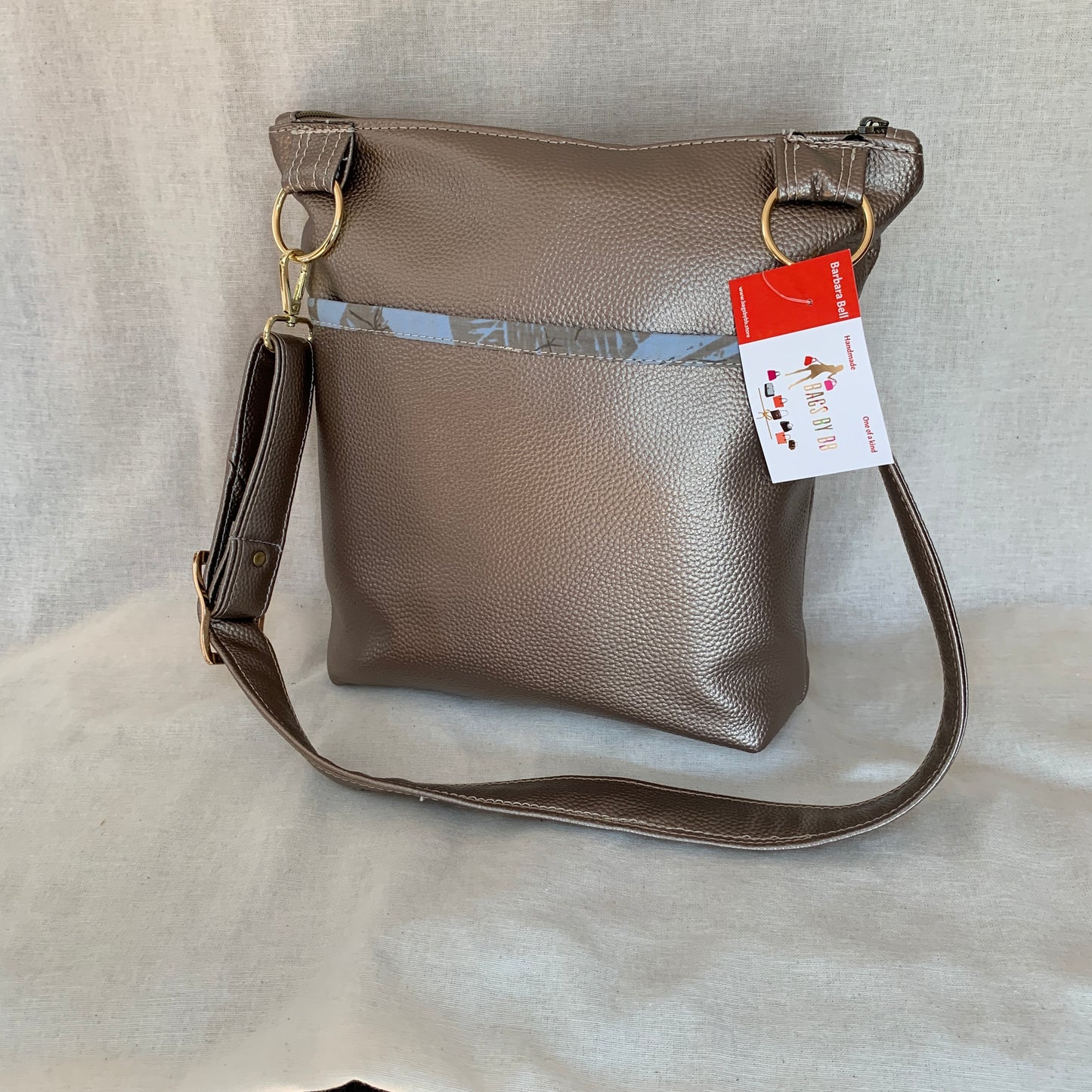 Metallic vinyl crossbody with exterior slip pockets and interior zip pockets.
