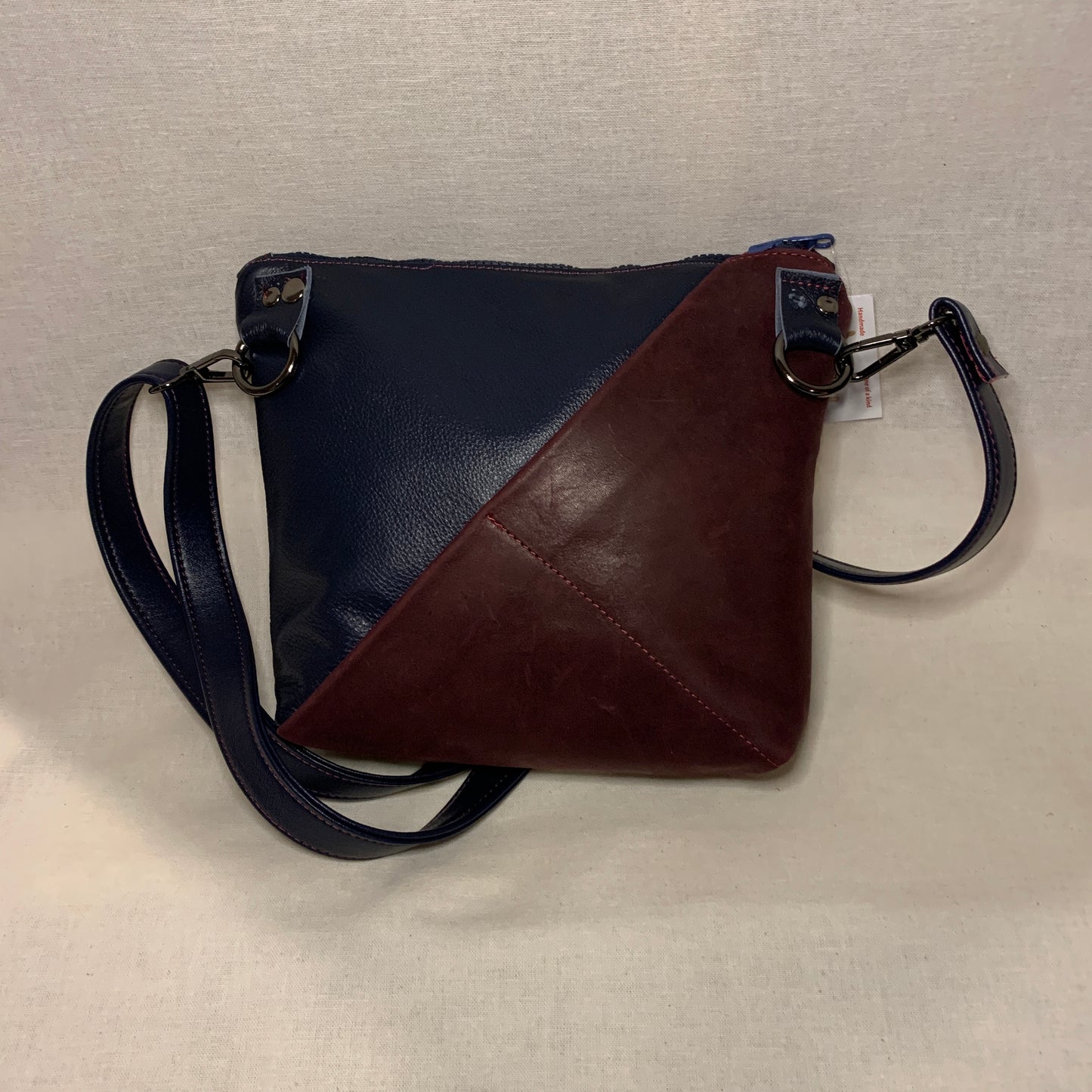 Classically designed all leather crossbody bag with burgundy and navy stripes.